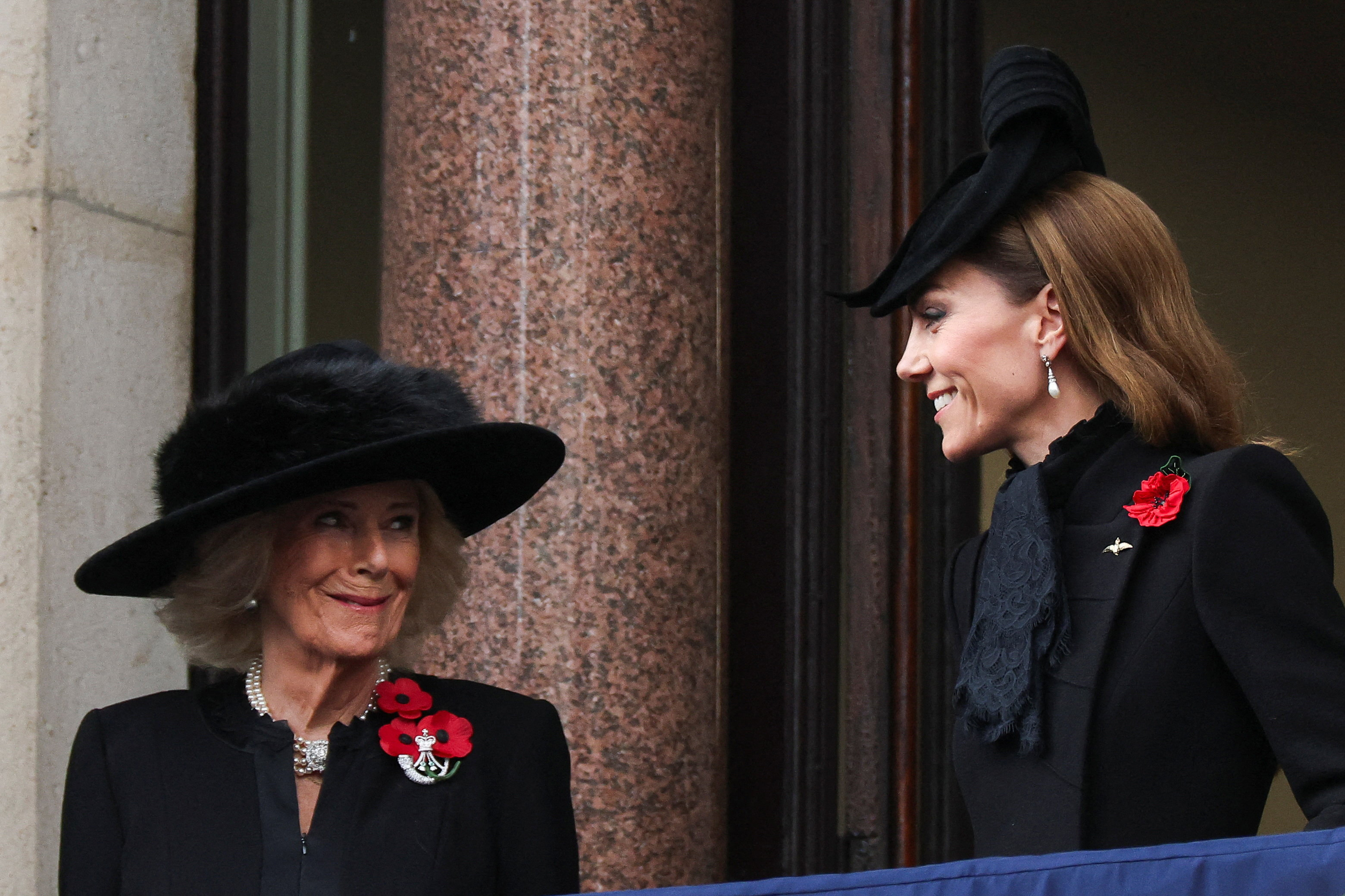 Princess Kate Middleton has long wavy brown hair and stands next to Queen Camilla