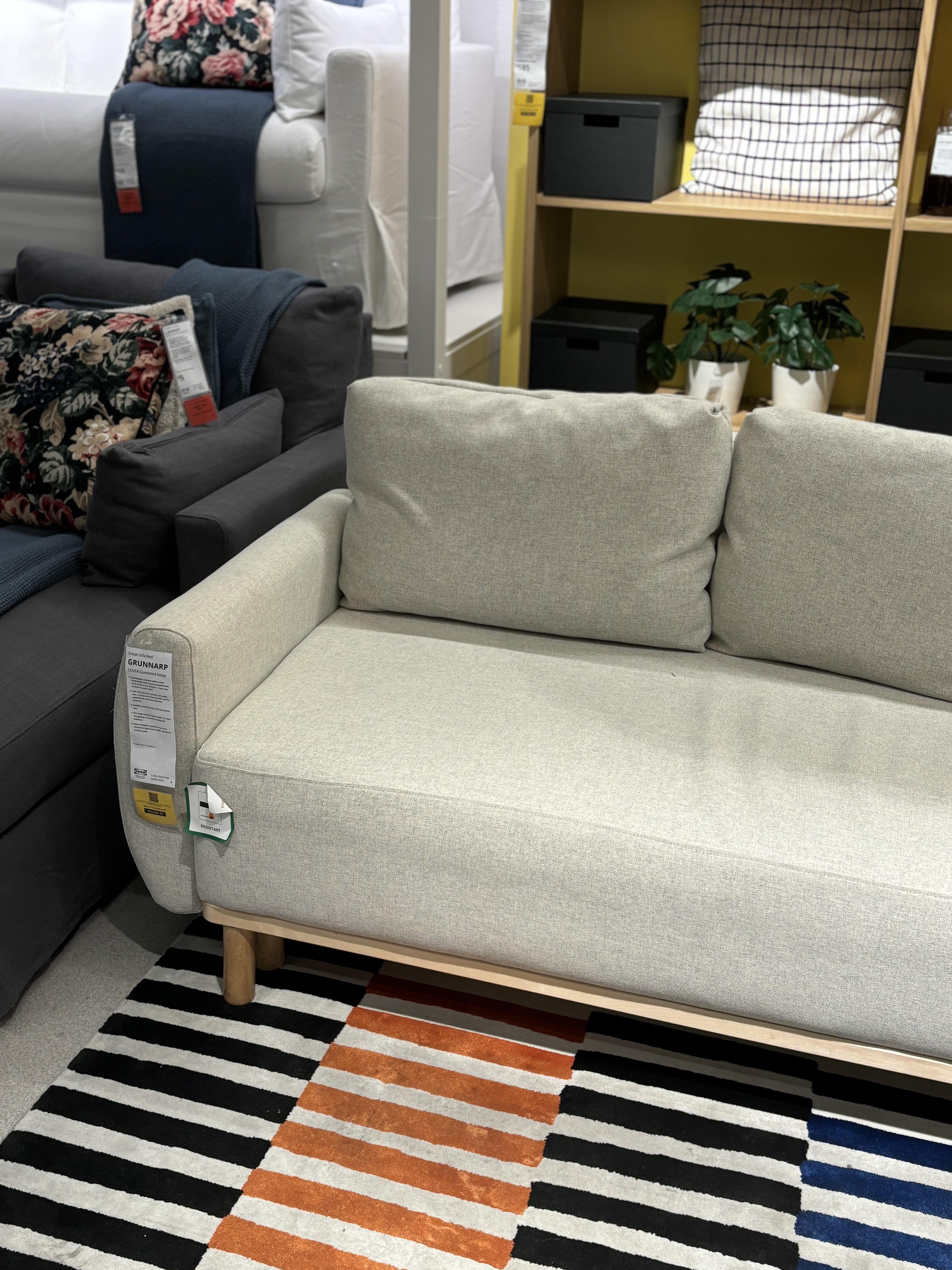 a photo of a tan sofa in a showroom, situated on a black, orange, blue and white striped rug.