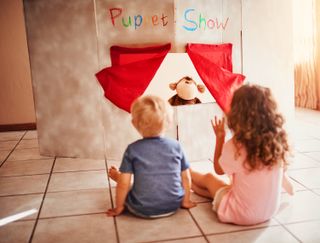 Shot of two little siblings sat facing and watching a puppet show at home.