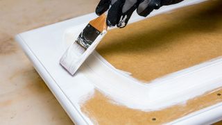 Gloved hand using paintbrush to paint kitchen cabinet door