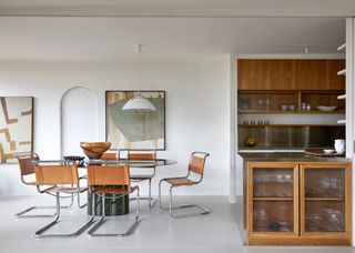 Fluted glass kitchen cabinets on the right and on the left is a dining table and chairs. Artwork also hangs on the wall of this open plan kitchen.