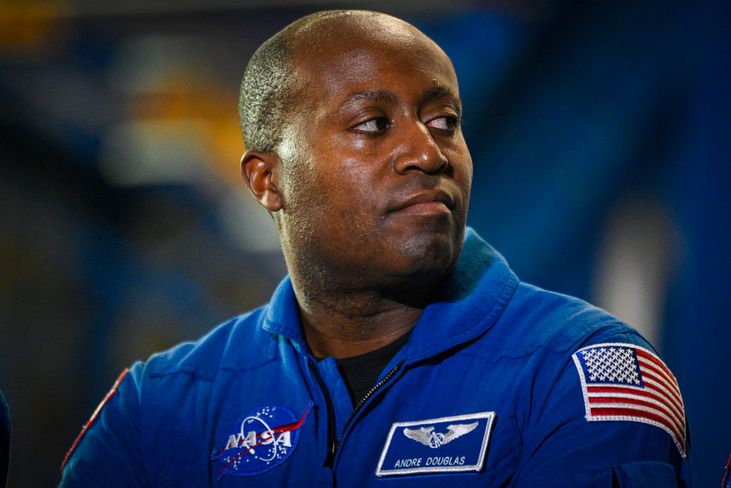 An African American man wearing a blue jumpsuit looks to the right of the camera.