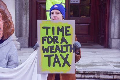 An activist holds a 'Time for a wealth tax' placard