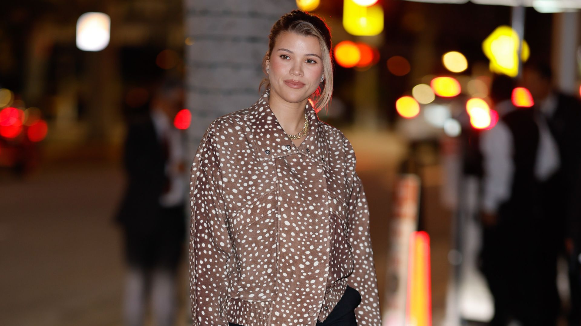 Sofia Richie walks down the street wearing black trousers with snakeskin heels and a deer print jacket.