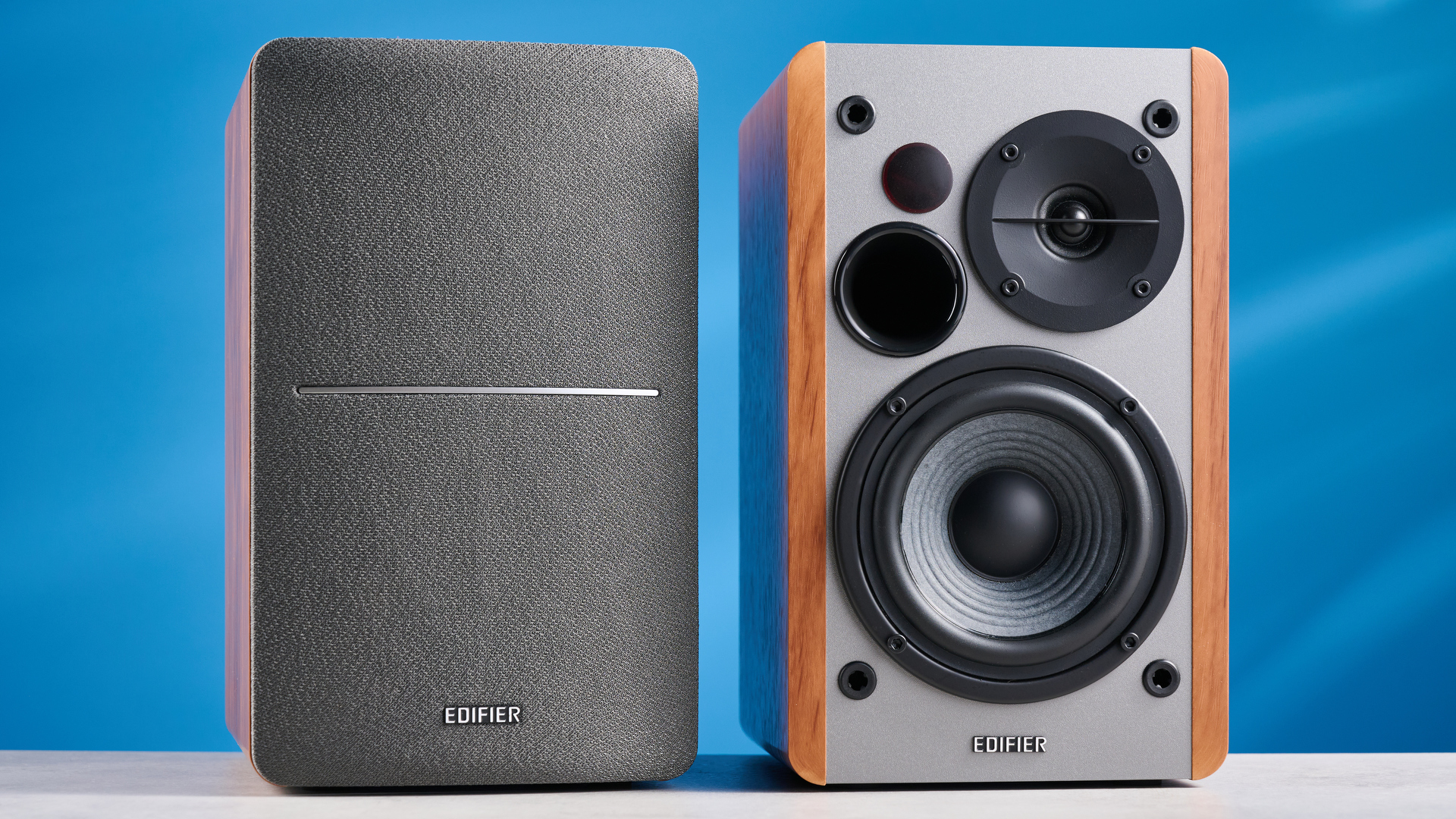the edifier r1280t bookshelf speakers in wood brown photographed against the blue background, showing the volume adjustment dials, internal drivers and tweeters, RCA and aux inputs, and remote