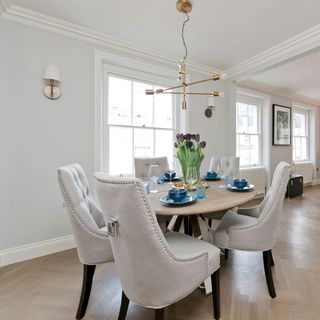 Round wooden dining table with 5 grey upholstered chairs and a modern brass light hanging from the ceiling
