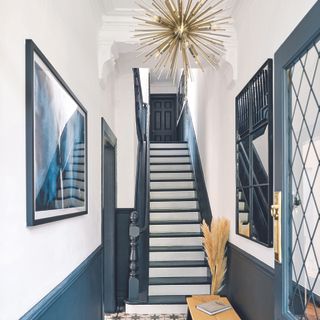 Narrow hallway with navy panelling, patterned navy and white tiled floors and a navy front door.