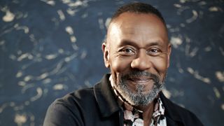 Sir Lenny Henry in a black top and black and white shirt smiles at the camera for Lenny Henry: One of a Kind.
