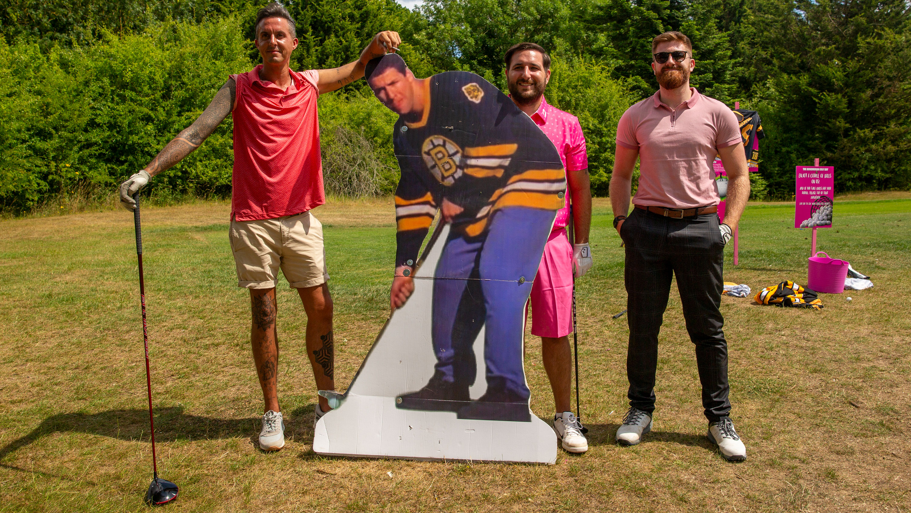 three golfers wear pink and stand behind a cut out of Happy Gilmore on a charity golf day, indicating a fun competition to include 