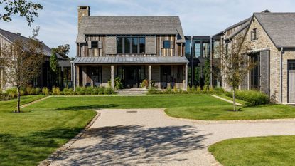 Exterior shot of large stone fronted home with covered porch, with manicured front lawn and driveway