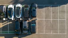 Various types of cars parked in a parking lot, seen from aerial view.