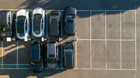 Various types of cars parked in a parking lot, seen from aerial view.