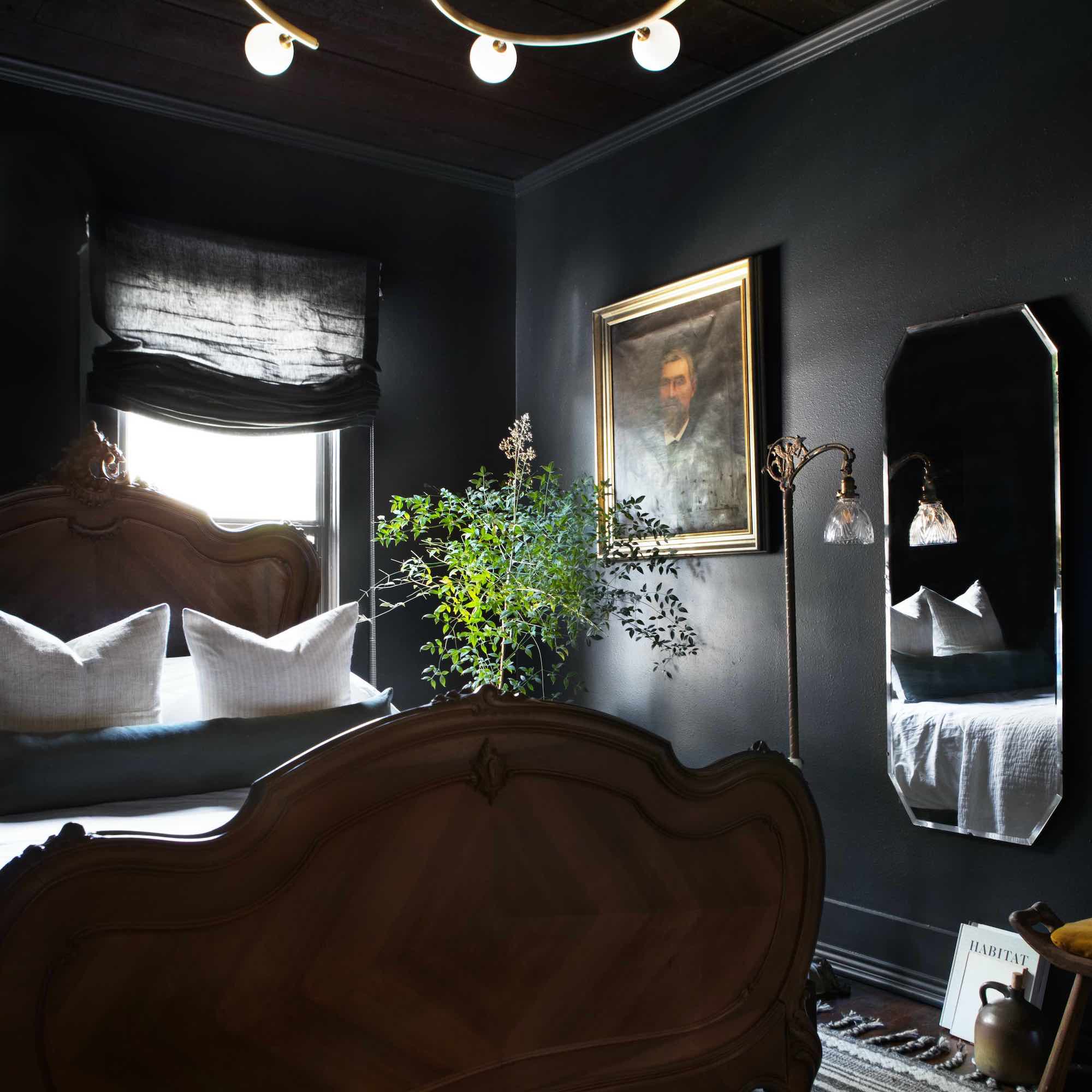 bedroom drenched in black paint with big wooden bed, mirror and oil painting on wall