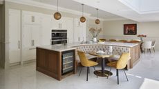 A kitchen with white inset cabinetry and a large island with built-in banquette bench seating and a wine fridge at the end of the unit