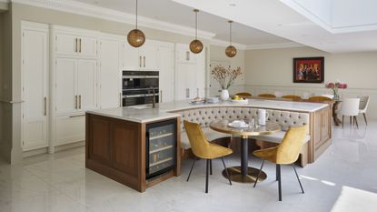 A kitchen with white inset cabinetry and a large island with built-in banquette bench seating and a wine fridge at the end of the unit