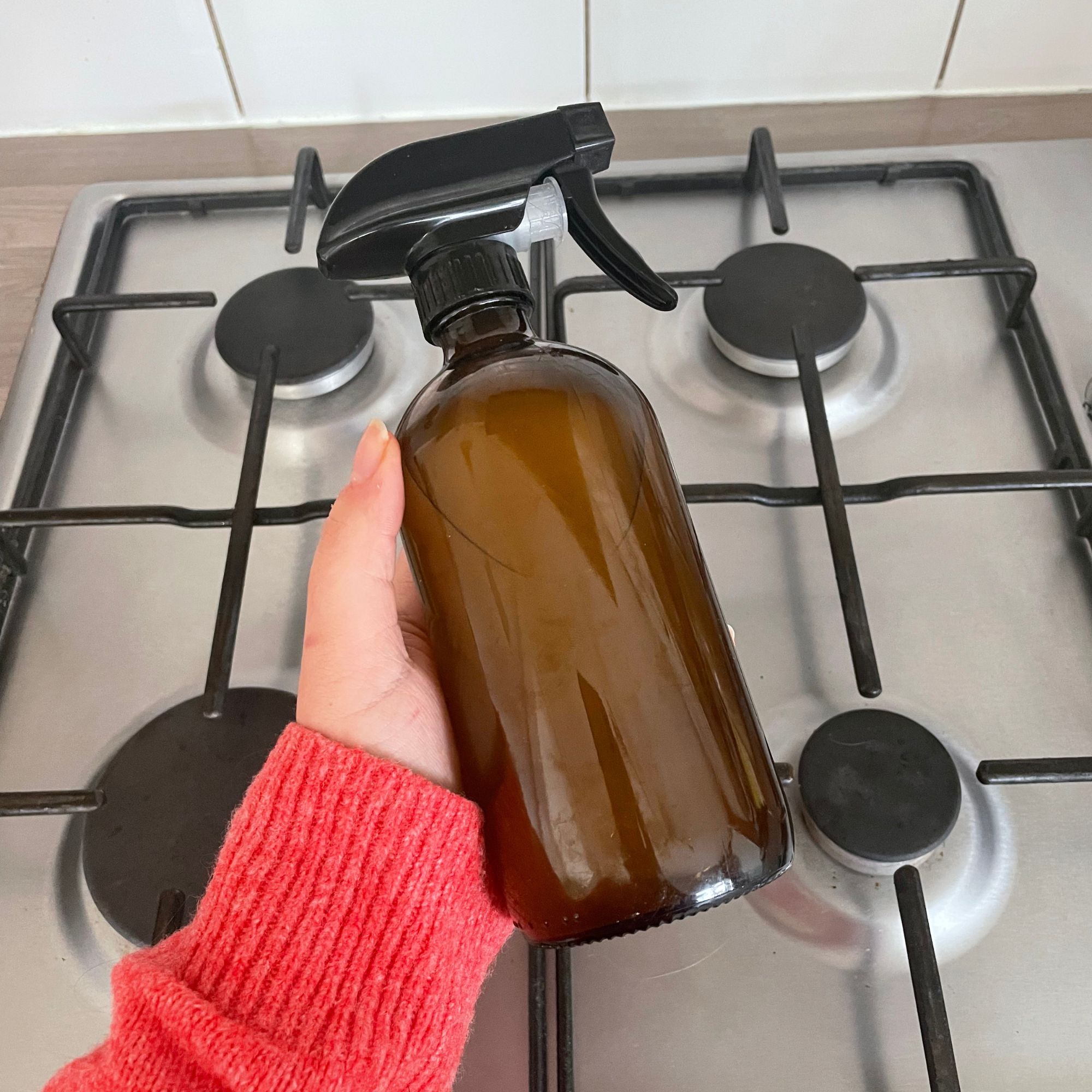 Hand holding a brown bottle of rice water over a hob
