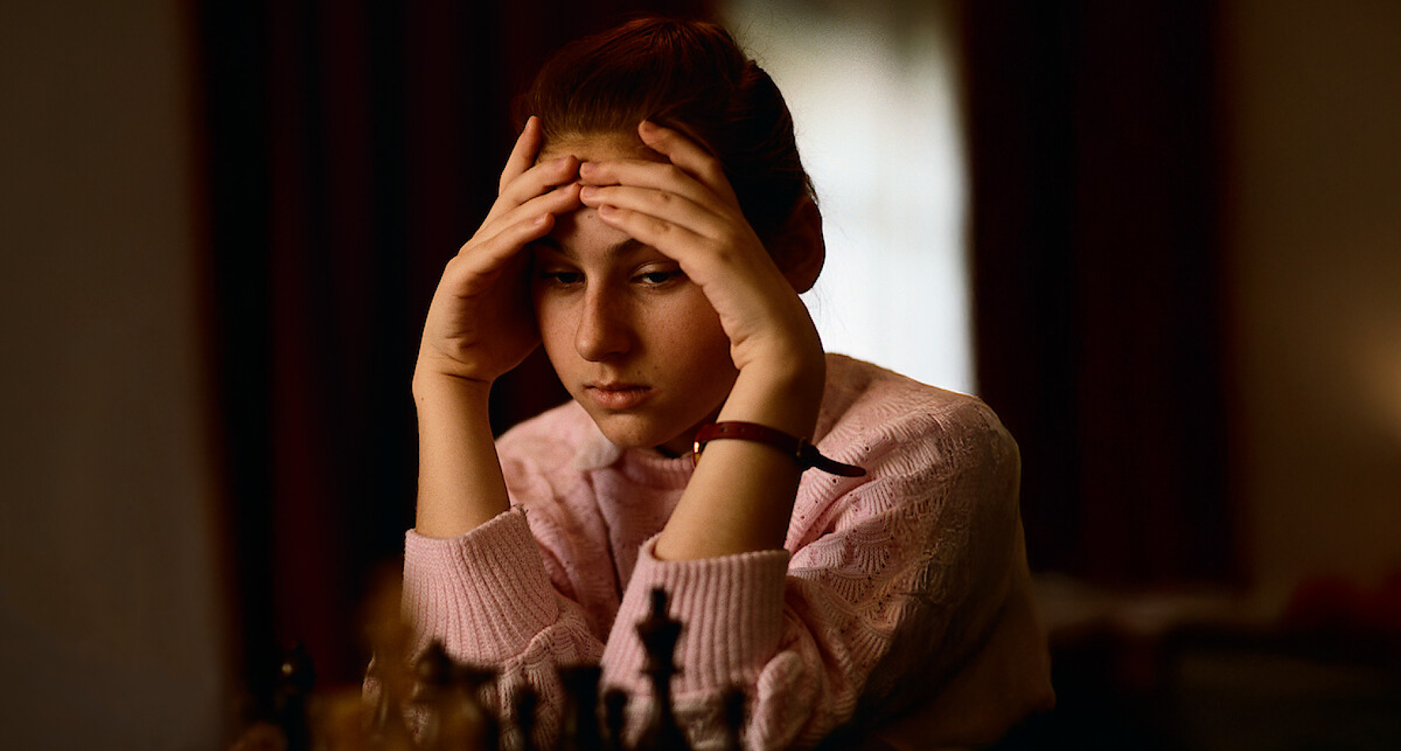 a young girl chess prodigy rests her head in her hands while playing chess in a still from the documentary queen of chess