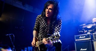 Steve Stevens wears a polka-dot shit and plays his Knaggs single-cut on a stage lit up in blue, Marshall stacks in the background.