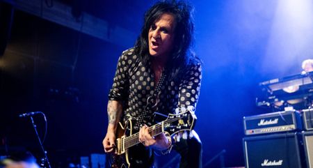 Steve Stevens wears a polka-dot shit and plays his Knaggs single-cut on a stage lit up in blue, Marshall stacks in the background.