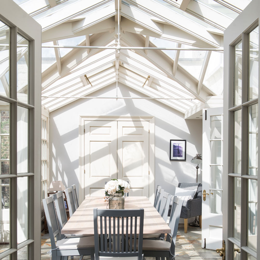 A bright and airy conservatory with a dining table and grey chairs