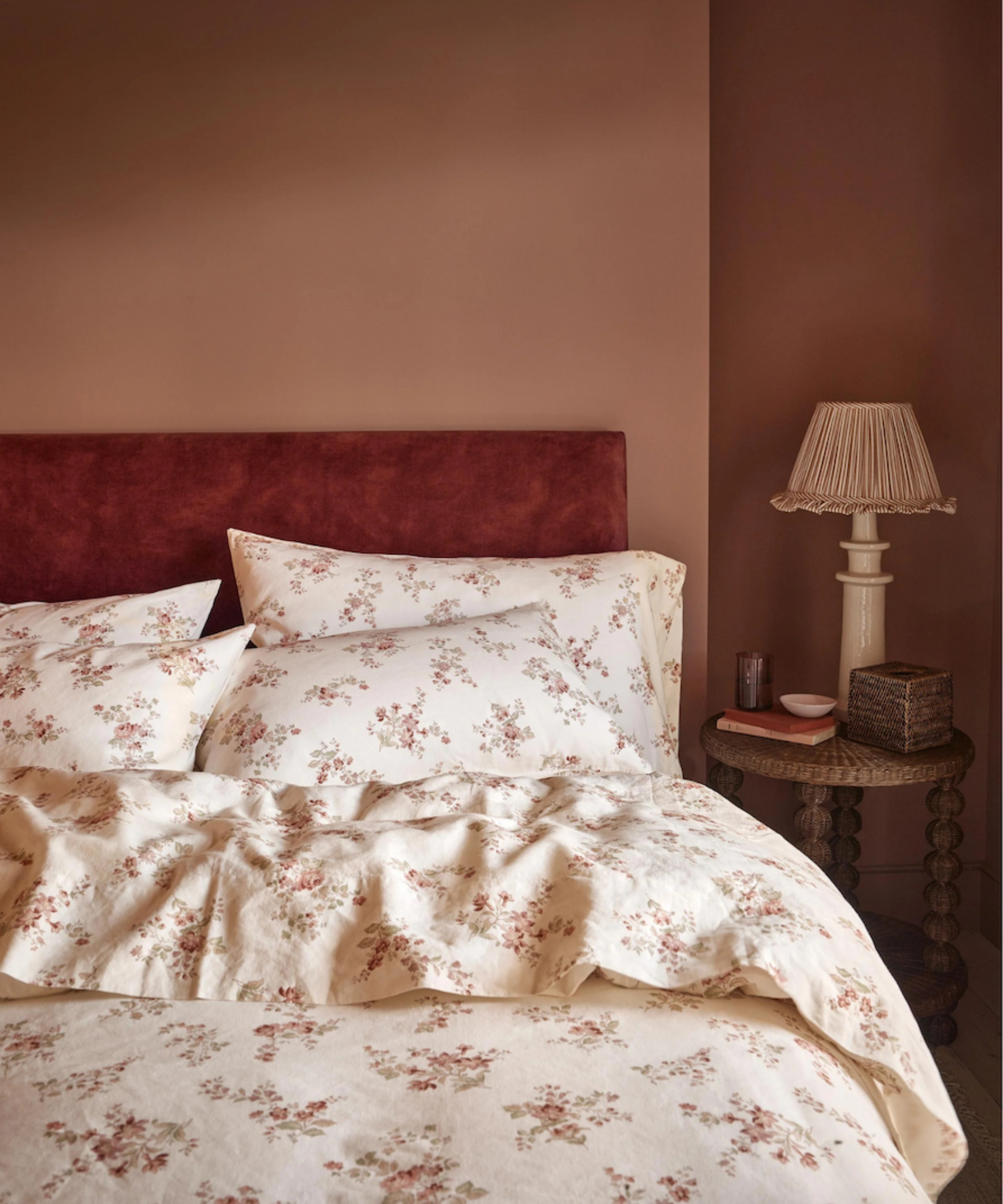 Moody blush pink bedroom with an oxblood bed frame and coordinating antique floral bed sheets