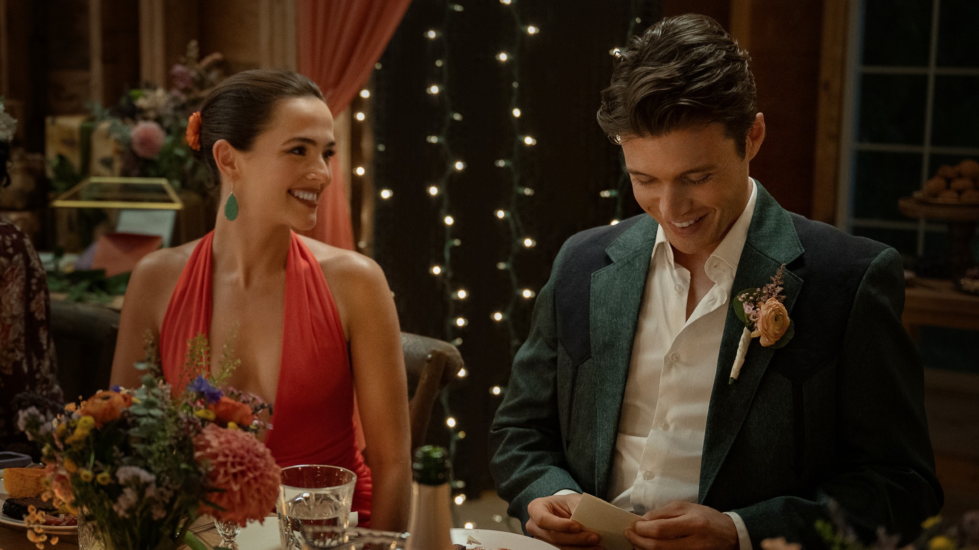 (L-R) Zoey Deutch as Jill and Nick Robinson as Wes sitting together at a fancy table. She's smiling at him, while he looks down. 