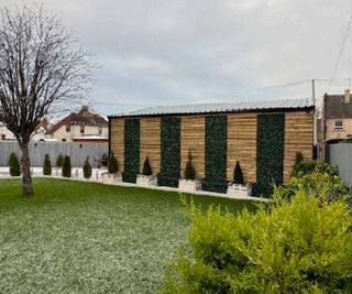 A garage with wooden cladding and artificial plants sitting next to a lawn