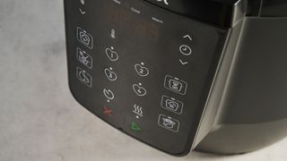 a black pressure cooker photographed against a blue background, showing its cooking presets, steam release valve, and Instant Pot branding