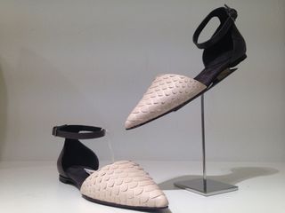 A pair of two-tone shoes in cream and black with one shoe displayed on a stand and the other shoe next to it