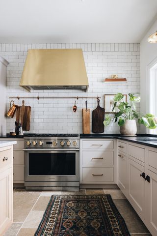 farmhouse kitchen with brass cooker hood white tiles and stone floor with rug