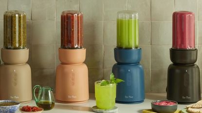 Four different colored Our Place Splendor Blenders in a row filled with smoothies. Left to right, taupe, orange, blye, and brown