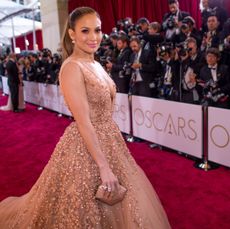 Jennifer Lopez wearing a tan sequined ball gown standing on the Oscars red carpet