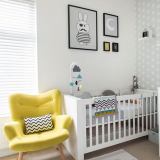 White nursery with cot, grey patterned wallpaper and yellow armchair