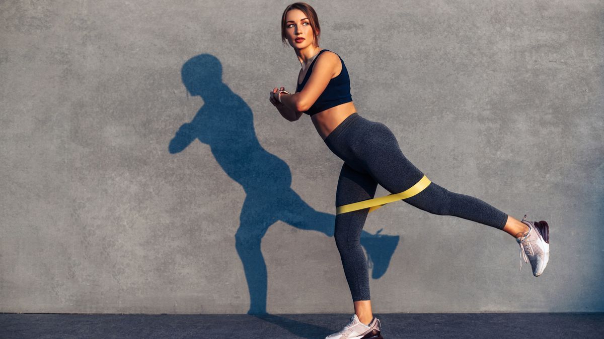 a woman performing a standing donkey kick with a resistance band around her legs