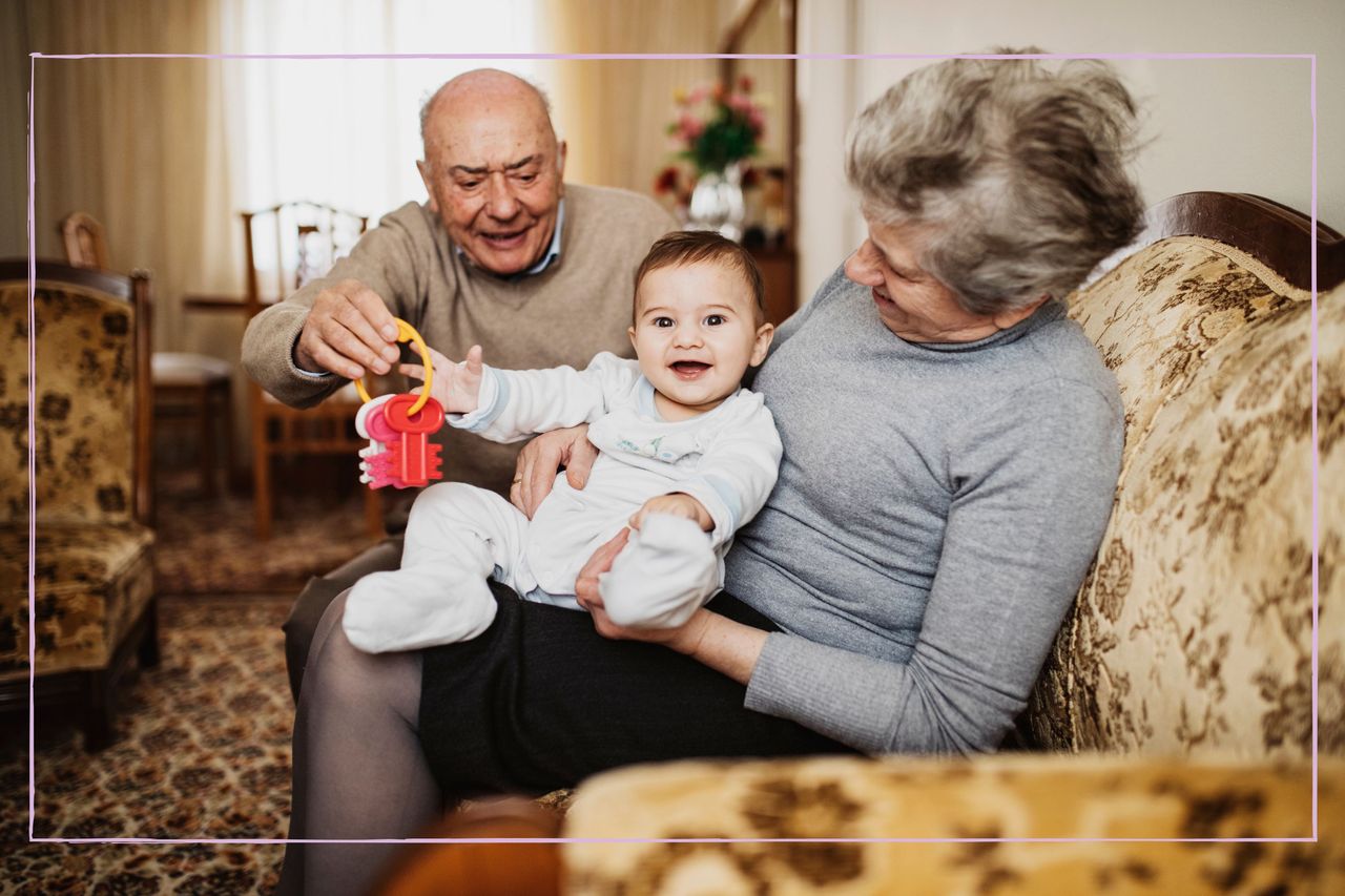 Grandparents sat on a sofa playing with a baby