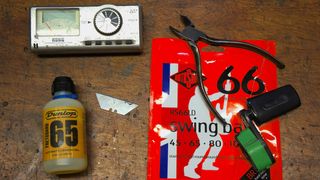 A tuner, bottle of oil, wire cutters, string winder and strings sat on a wooden desk