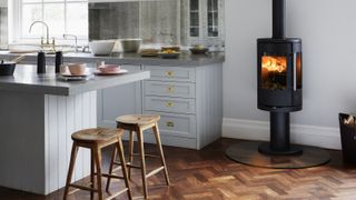 black freestanding log burner in open plan kitchen area with grey units and large kitchen island with stools at end of island