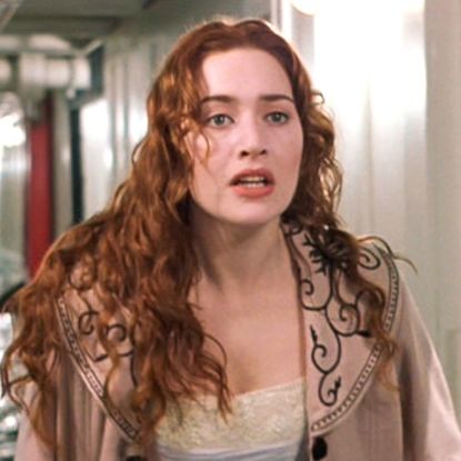 Kate Winslet standing in a flooded corridor in a still from the movie Titanic, her character has long red curly hair and she is wearing a tan coat with embroidered detailing on the collar