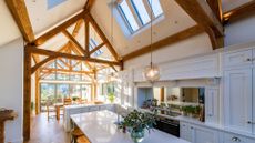 An open concept white dining and kitchen space with vaulted ceilings featuring open woodwork and overhead roof windows 