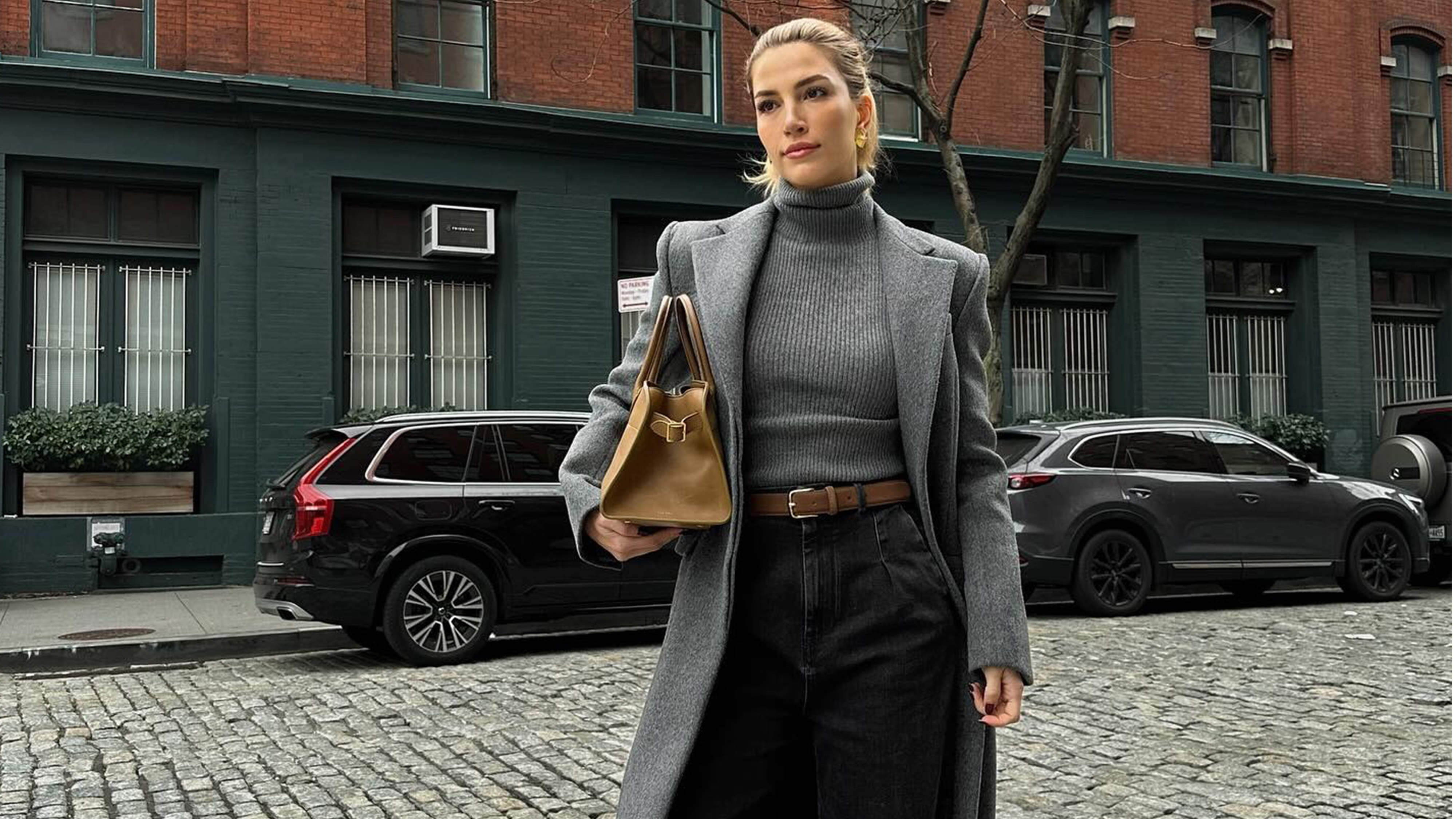 Cass wears a gray turtleneck, gray coat, beige belt, and black jeans.