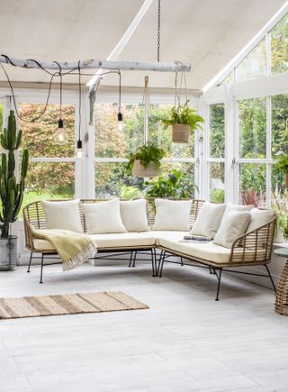a simple white rattan sofa, hanging plants and lights in a minimalistic orangery
