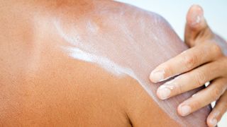 A woman applying sunscreen on her back