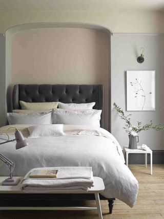 grey bedroom with grey button backed bed, wooden floor, alcove, side table, wall light, bench seat