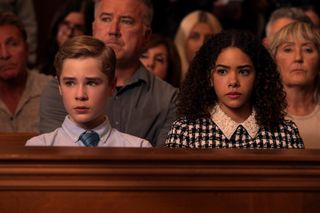 A teen boy and a teen girl sit in the front row of a court room audience, in 'Ginny and Georgia' season 3.