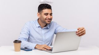 Smug-looking man wearing a sky blue shirt, looking at a laptop, with a halo above his head