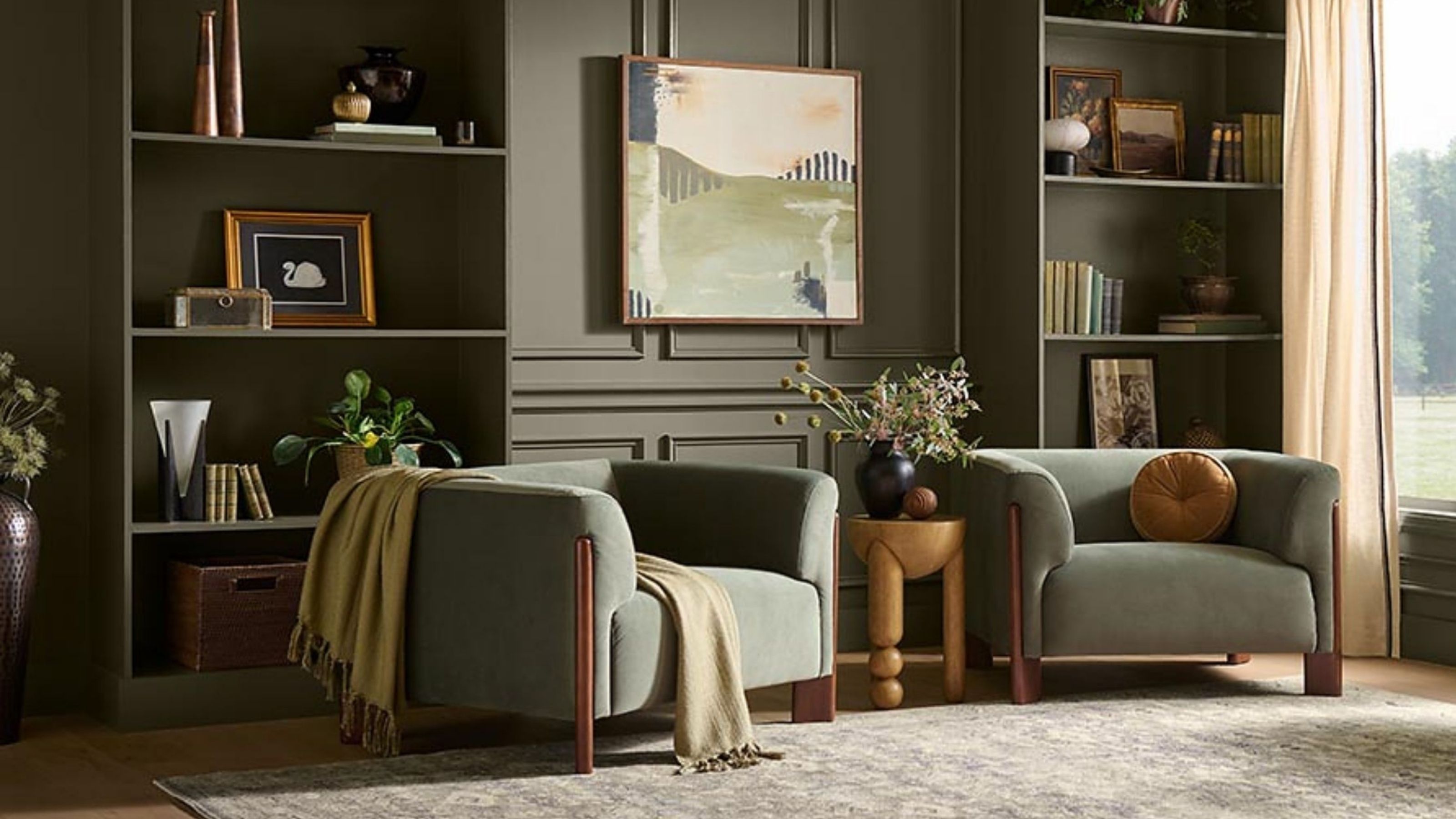Image of a large living room drenched in olive green with built-in bookshelves, two green accent chairs, a beige rug, and windows with off-white curtains.