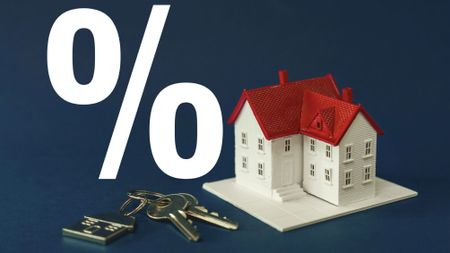 A tiny model home on a blue background with a large percent sign next to it and a set of keys. 