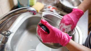 Someone cleaning a pot in a sink while wearing pink gloves