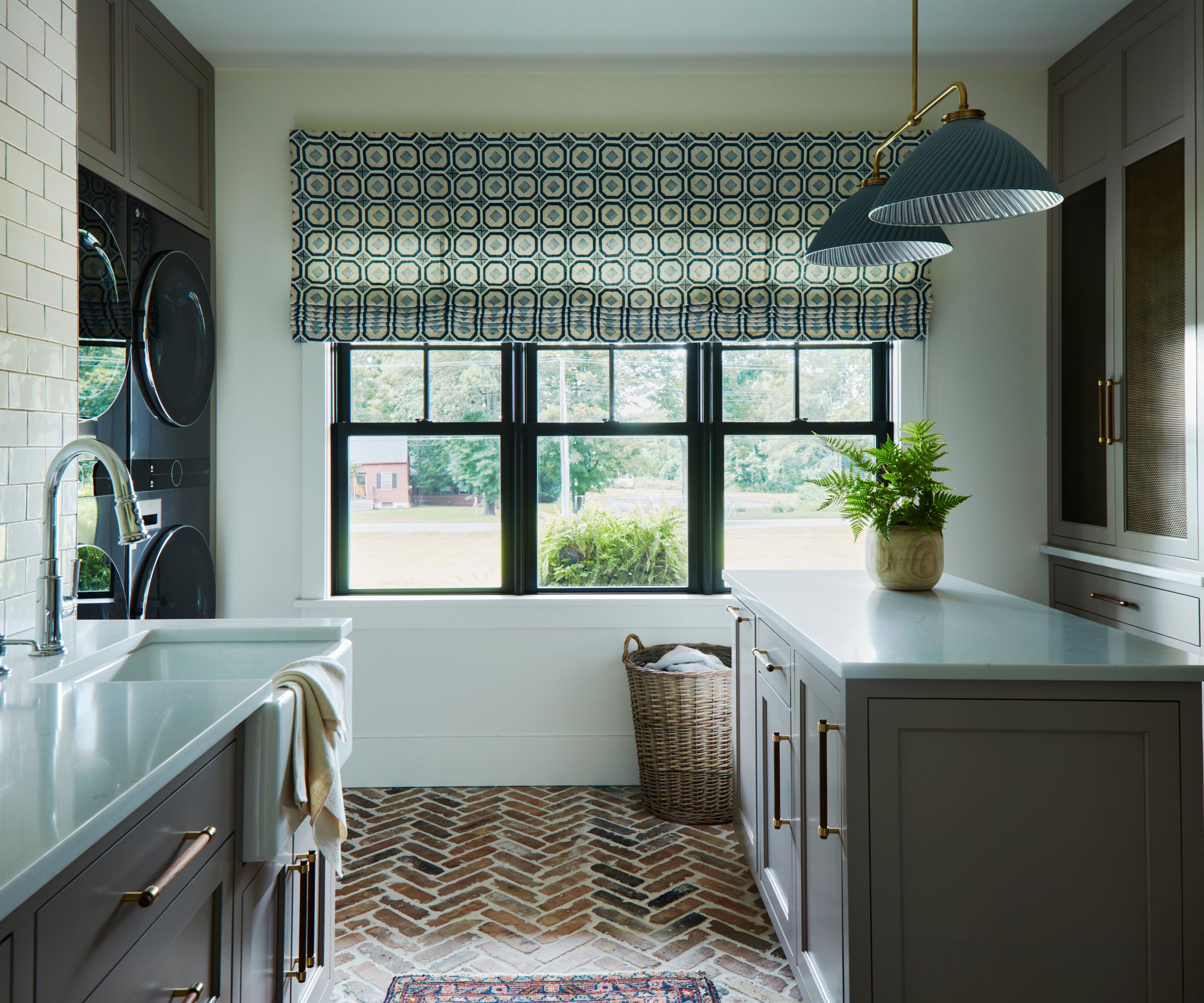 large laundry room with terracotta herringbone floor, dark mushroom gray cabinetry, a large island, and double washer dryers