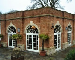 brickwork orangery with custom windows by Redwood Stone, and palm trees in pots outside the curved windows/doors